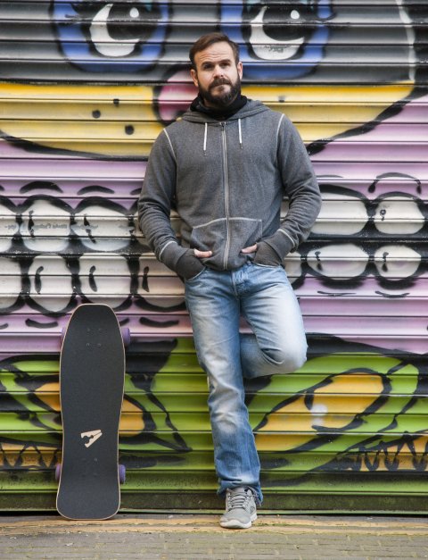 Male skateboarder leaning against shutter with street art by Sweet Toof, Rowdy and Shuby